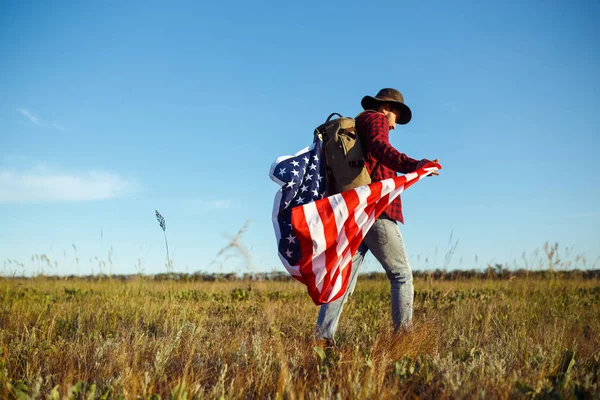 4 Temmuz. Amerikan Flag.Patriotic tatil. Amerika bayrağı ile seyahat. Adam bir şapka, bir sırt çantası, bir tişört ve kot pantolon giyiyor. Güzel gün batımı ışık. Amerikan tarzı. 