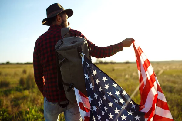 4 Temmuz. Amerikan Flag.Patriotic tatil. Amerika bayrağı ile seyahat. Adam bir şapka, bir sırt çantası, bir tişört ve kot pantolon giyiyor. Güzel gün batımı ışık. Amerikan tarzı. 