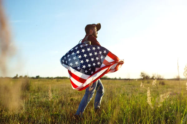 4 Temmuz. Amerikan Flag.Patriotic tatil. Amerika bayrağı ile seyahat. Adam bir şapka, bir sırt çantası, bir tişört ve kot pantolon giyiyor. Güzel gün batımı ışık. Amerikan tarzı. 