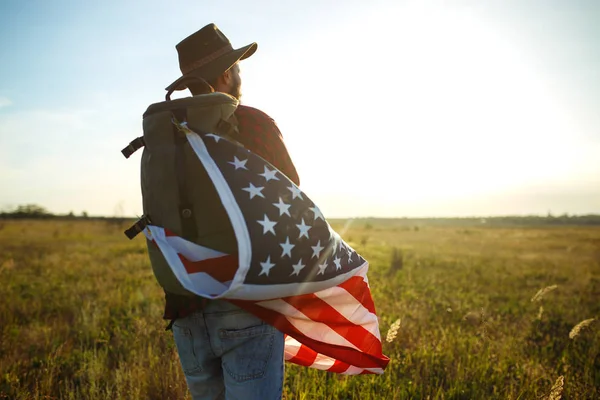 4 Temmuz. Amerikan Flag.Patriotic tatil. Amerika bayrağı ile seyahat. Adam bir şapka, bir sırt çantası, bir tişört ve kot pantolon giyiyor. Güzel gün batımı ışık. Amerikan tarzı. 
