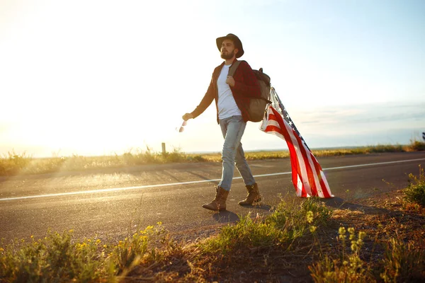 4 Temmuz. Amerikan Flag.Patriotic tatil. Amerika bayrağı ile seyahat. Adam bir şapka, bir sırt çantası, bir tişört ve kot pantolon giyiyor. Güzel gün batımı ışık. Amerikan tarzı. 