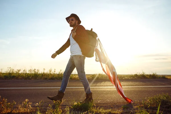4 Temmuz. Amerikan Flag.Patriotic tatil. Amerika bayrağı ile seyahat. Adam bir şapka, bir sırt çantası, bir tişört ve kot pantolon giyiyor. Güzel gün batımı ışık. Amerikan tarzı. 