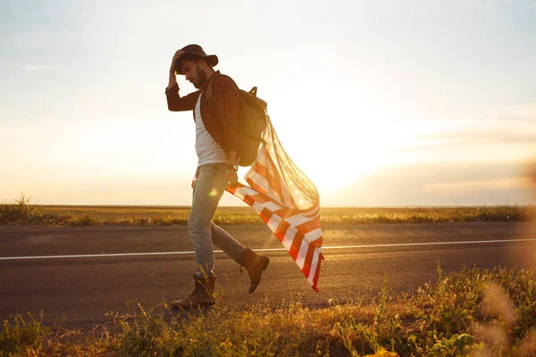 4 Temmuz. Amerikan Flag.Patriotic tatil. Amerika bayrağı ile seyahat. Adam bir şapka, bir sırt çantası, bir tişört ve kot pantolon giyiyor. Güzel gün batımı ışık. Amerikan tarzı. 