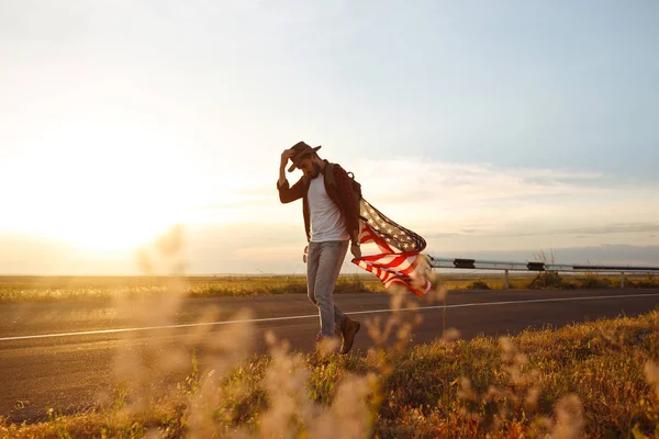 4 Temmuz. Amerikan Flag.Patriotic tatil. Amerika bayrağı ile seyahat. Adam bir şapka, bir sırt çantası, bir tişört ve kot pantolon giyiyor. Güzel gün batımı ışık. Amerikan tarzı. 