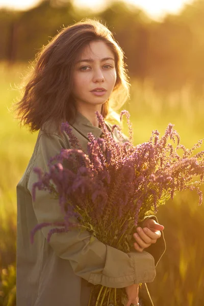 Portrait of a beautiful girl with a bouquet of lavender. Sunset light and beautiful sensuality. The girl is enjoying the moment. The concept of beauty. Summer sunset light, wonderful atmosphere