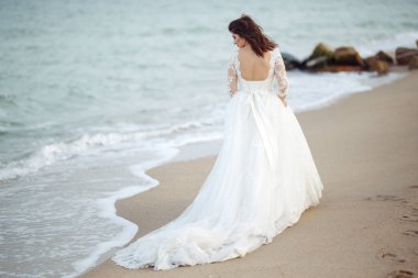 Beyaz bir gelinlikle çok güzel bir gelin sahilde yürüyor. Dalgalar elbisesini yakınındaki. Güzel gün batımı atmosfer, yaz gecesi. Düğün kavramı