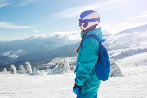 A beautiful girl in winter clothes, a blue helmet and a green jacket is having a great time in the mountains. Concept of travel, leisure, freedom, sport. Beautiful nature, places, great weather.