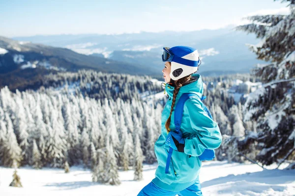 A beautiful girl in winter clothes, a blue helmet and a green jacket is having a great time in the mountains. Concept of travel, leisure, freedom, sport. Beautiful nature, places, great weather.