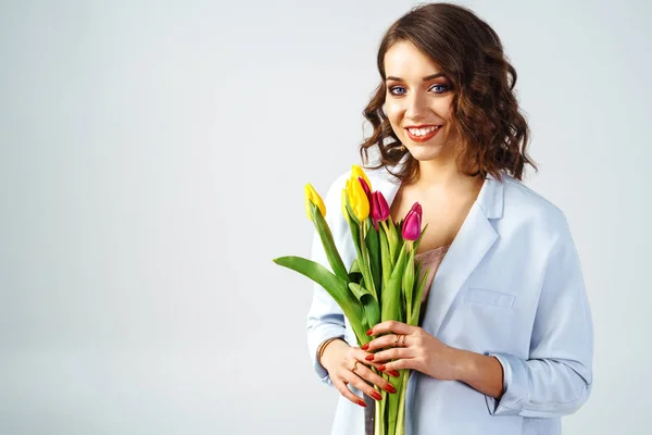 Fashion photo of a beautiful young woman with tulips in her hand .she dressed in a beautiful coat, and T-shirt with stripes.Spring concept. March 8. beautiful girl in stylish clothes