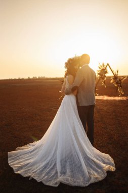 genç ve güzel gelin ve damat hoşlanıyoruz. Düğün günü boho tarzı. Mutlu gelin ve damat açık doğa gün batımında güneş portresi. Sıcak yaz.