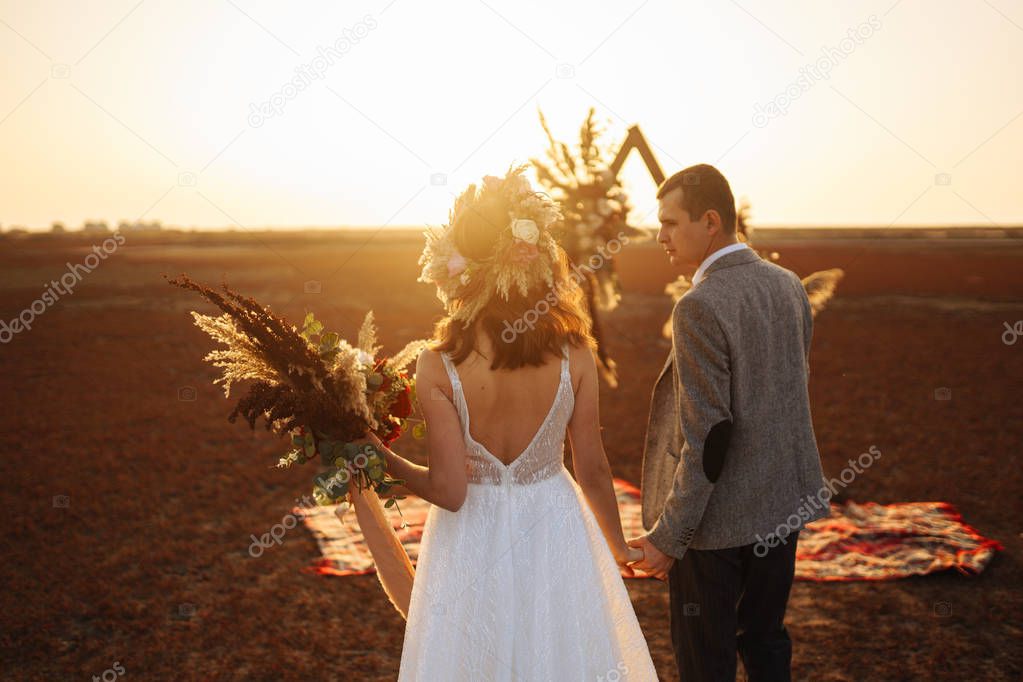 young and beautiful bride and groom enjoy each other. Wedding day in boho style. Sunshine portrait of happy bride and groom outdoor in nature at sunset. Warm summertime.