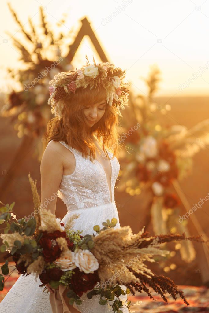 Amazing bride in sunset light. Pretty bride. Boho style. Bride wearing fashion wedding dress with feathers with luxury delight make-up and hairstyle.