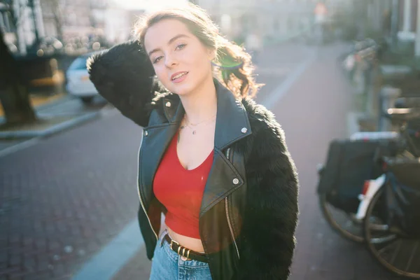 一个美丽的女孩在阳光明媚的日子的肖像 阿姆斯特丹的街道 很好的心情 一个女孩喜欢她的生活方式 她穿着一件红色的 牛仔裤和一件皮夹克 — 图库照片