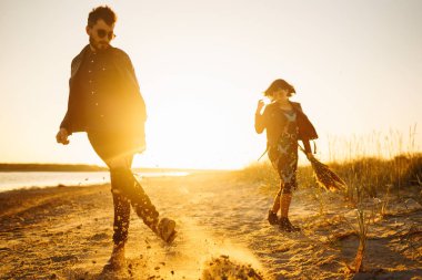 Birlikte eğleniyoruz. Tarz sahibi ve sevgi dolu bir çift deniz kenarında eğleniyor. Çift genç ve aşıklar. Gençlik, aşk ve yaşam tarzı kavramı. Güzel bir yaz gününde gün batımı.