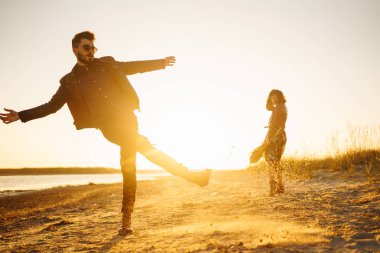 Birlikte eğleniyoruz. Tarz sahibi ve sevgi dolu bir çift deniz kenarında eğleniyor. Çift genç ve aşıklar. Gençlik, aşk ve yaşam tarzı kavramı. Güzel bir yaz gününde gün batımı.