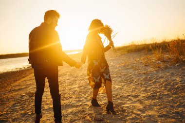 Birlikte eğleniyoruz. Tarz sahibi ve sevgi dolu bir çift deniz kenarında eğleniyor. Çift genç ve aşıklar. Gençlik, aşk ve yaşam tarzı kavramı. Güzel bir yaz gününde gün batımı.