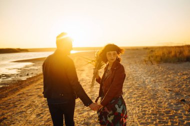 Birlikte eğleniyoruz. Tarz sahibi ve sevgi dolu bir çift deniz kenarında eğleniyor. Çift genç ve aşıklar. Gençlik, aşk ve yaşam tarzı kavramı. Güzel bir yaz gününde gün batımı.