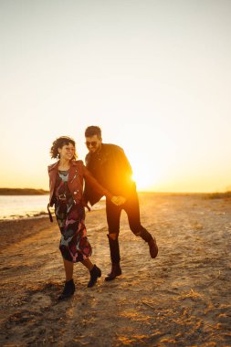 Birlikte eğleniyoruz. Tarz sahibi ve sevgi dolu bir çift deniz kenarında eğleniyor. Çift genç ve aşıklar. Gençlik, aşk ve yaşam tarzı kavramı. Güzel bir yaz gününde gün batımı.