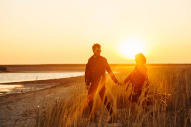 Birlikte eğleniyoruz. Tarz sahibi ve sevgi dolu bir çift deniz kenarında eğleniyor. Çift genç ve aşıklar. Gençlik, aşk ve yaşam tarzı kavramı. Güzel bir yaz gününde gün batımı.