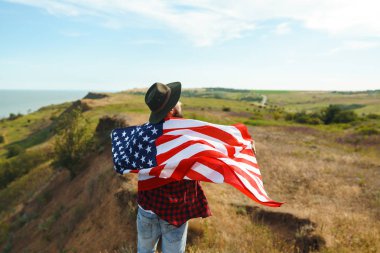 4 Temmuz. 4 Temmuz. Ulusal bayrağı olan Amerikalı. Amerikan bayrağı. Bağımsızlık günü. Vatanseverlik tatili. Adam şapka, sırt çantası, gömlek ve kot giyiyor. Güzel günbatımı ışık. 