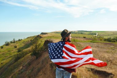 4 Temmuz. 4 Temmuz. Ulusal bayrağı olan Amerikalı. Amerikan bayrağı. Bağımsızlık günü. Vatanseverlik tatili. Adam şapka, sırt çantası, gömlek ve kot giyiyor. Güzel günbatımı ışık. 
