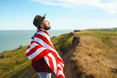 4 Temmuz. 4 Temmuz. Ulusal bayrağı olan Amerikalı. Amerikan bayrağı. Bağımsızlık günü. Vatanseverlik tatili. Adam şapka, sırt çantası, gömlek ve kot giyiyor. Güzel günbatımı ışık. 