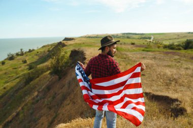 4 Temmuz. 4 Temmuz. Ulusal bayrağı olan Amerikalı. Amerikan bayrağı. Bağımsızlık günü. Vatanseverlik tatili. Adam şapka, sırt çantası, gömlek ve kot giyiyor. Güzel günbatımı ışık. 