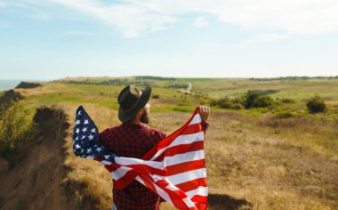 4 Temmuz. 4 Temmuz. Ulusal bayrağı olan Amerikalı. Amerikan bayrağı. Bağımsızlık günü. Vatanseverlik tatili. Adam şapka, sırt çantası, gömlek ve kot giyiyor. Güzel günbatımı ışık. 