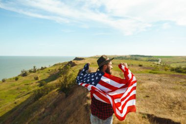 4 Temmuz. 4 Temmuz. Ulusal bayrağı olan Amerikalı. Amerikan bayrağı. Bağımsızlık günü. Vatanseverlik tatili. Adam şapka, sırt çantası, gömlek ve kot giyiyor. Güzel günbatımı ışık. 