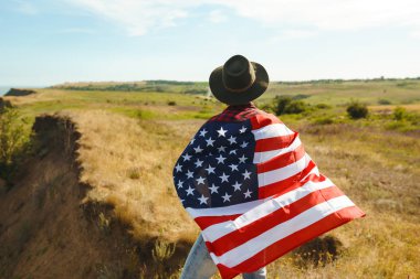 4 Temmuz. 4 Temmuz. Ulusal bayrağı olan Amerikalı. Amerikan bayrağı. Bağımsızlık günü. Vatanseverlik tatili. Adam şapka, sırt çantası, gömlek ve kot giyiyor. Güzel günbatımı ışık. 
