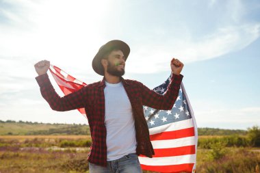 4 Temmuz. 4 Temmuz. Ulusal bayrağı olan Amerikalı. Amerikan bayrağı. Bağımsızlık günü. Vatanseverlik tatili. Adam şapka, sırt çantası, gömlek ve kot giyiyor. Güzel günbatımı ışık. 