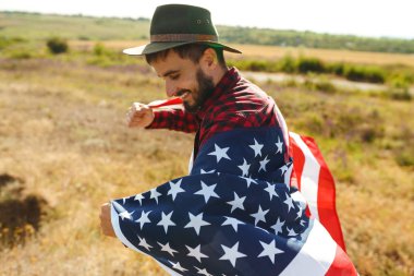 4 Temmuz. 4 Temmuz. Ulusal bayrağı olan Amerikalı. Amerikan bayrağı. Bağımsızlık günü. Vatanseverlik tatili. Adam şapka, sırt çantası, gömlek ve kot giyiyor. Güzel günbatımı ışık. 