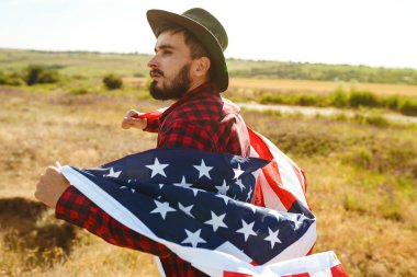 4 Temmuz. 4 Temmuz. Ulusal bayrağı olan Amerikalı. Amerikan bayrağı. Bağımsızlık günü. Vatanseverlik tatili. Adam şapka, sırt çantası, gömlek ve kot giyiyor. Güzel günbatımı ışık. 