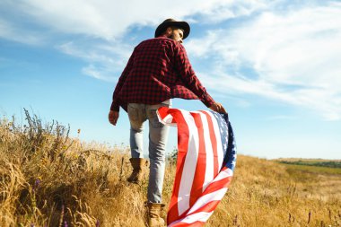 4 Temmuz. 4 Temmuz. Ulusal bayrağı olan Amerikalı. Amerikan bayrağı. Bağımsızlık günü. Vatanseverlik tatili. Adam şapka, sırt çantası, gömlek ve kot giyiyor. Güzel günbatımı ışık. 