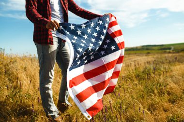 4 Temmuz. 4 Temmuz. Ulusal bayrağı olan Amerikalı. Amerikan bayrağı. Bağımsızlık günü. Vatanseverlik tatili. Adam şapka, sırt çantası, gömlek ve kot giyiyor. Güzel günbatımı ışık. 