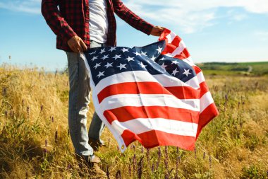 4 Temmuz. 4 Temmuz. Ulusal bayrağı olan Amerikalı. Amerikan bayrağı. Bağımsızlık günü. Vatanseverlik tatili. Adam şapka, sırt çantası, gömlek ve kot giyiyor. Güzel günbatımı ışık. 