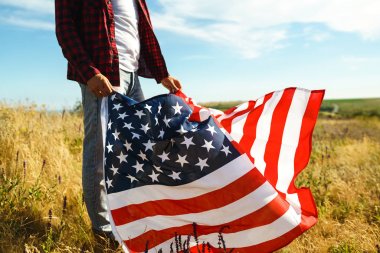 4 Temmuz. 4 Temmuz. Ulusal bayrağı olan Amerikalı. Amerikan bayrağı. Bağımsızlık günü. Vatanseverlik tatili. Adam şapka, sırt çantası, gömlek ve kot giyiyor. Güzel günbatımı ışık. 