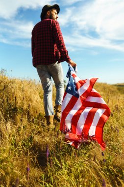 4 Temmuz. 4 Temmuz. Ulusal bayrağı olan Amerikalı. Amerikan bayrağı. Bağımsızlık günü. Vatanseverlik tatili. Adam şapka, sırt çantası, gömlek ve kot giyiyor. Güzel günbatımı ışık. 