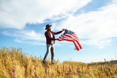 4 Temmuz. 4 Temmuz. Ulusal bayrağı olan Amerikalı. Amerikan bayrağı. Bağımsızlık günü. Vatanseverlik tatili. Adam şapka, sırt çantası, gömlek ve kot giyiyor. Güzel günbatımı ışık. 
