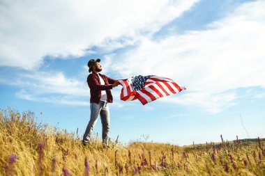 4 Temmuz. 4 Temmuz. Ulusal bayrağı olan Amerikalı. Amerikan bayrağı. Bağımsızlık günü. Vatanseverlik tatili. Adam şapka, sırt çantası, gömlek ve kot giyiyor. Güzel günbatımı ışık. 