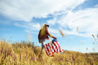 4 Temmuz. 4 Temmuz. Ulusal bayrağı olan Amerikalı. Amerikan bayrağı. Bağımsızlık günü. Vatanseverlik tatili. Adam şapka, sırt çantası, gömlek ve kot giyiyor. Güzel günbatımı ışık. 