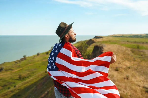 4 Temmuz. 4 Temmuz. Ulusal bayrağı olan Amerikalı. Amerikan bayrağı. Bağımsızlık günü. Vatanseverlik tatili. Adam şapka, sırt çantası, gömlek ve kot giyiyor. Güzel günbatımı ışık. 