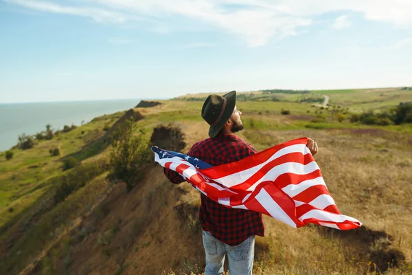 4 Temmuz. 4 Temmuz. Ulusal bayrağı olan Amerikalı. Amerikan bayrağı. Bağımsızlık günü. Vatanseverlik tatili. Adam şapka, sırt çantası, gömlek ve kot giyiyor. Güzel günbatımı ışık. 