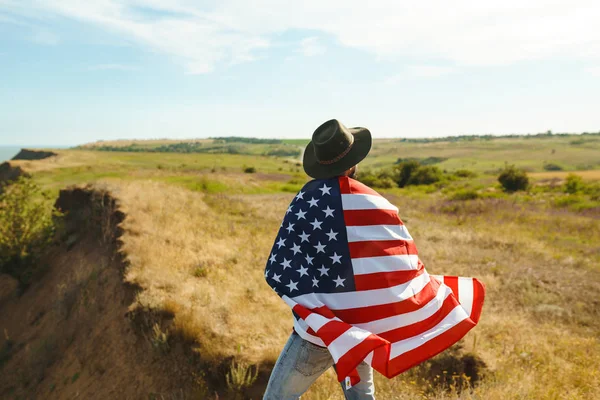 4 Temmuz. 4 Temmuz. Ulusal bayrağı olan Amerikalı. Amerikan bayrağı. Bağımsızlık günü. Vatanseverlik tatili. Adam şapka, sırt çantası, gömlek ve kot giyiyor. Güzel günbatımı ışık. 