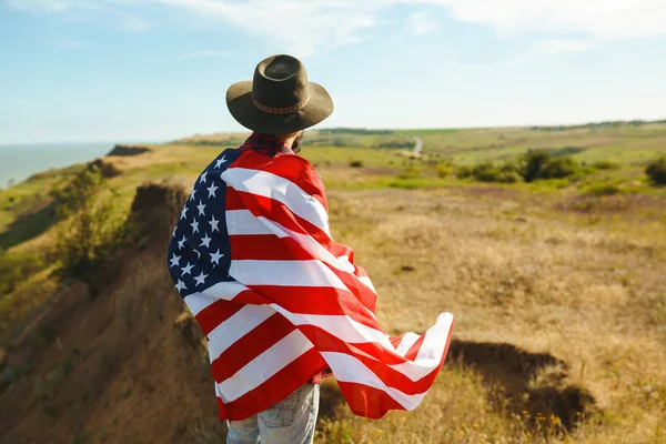 4 Temmuz. 4 Temmuz. Ulusal bayrağı olan Amerikalı. Amerikan bayrağı. Bağımsızlık günü. Vatanseverlik tatili. Adam şapka, sırt çantası, gömlek ve kot giyiyor. Güzel günbatımı ışık. 