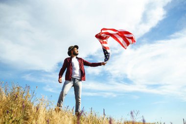 4 Temmuz. 4 Temmuz. Ulusal bayrağı olan Amerikalı. Amerikan bayrağı. Bağımsızlık günü. Vatanseverlik tatili. Adam şapka, sırt çantası, gömlek ve kot giyiyor. Güzel günbatımı ışık. 