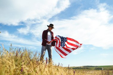 4 Temmuz. 4 Temmuz. Ulusal bayrağı olan Amerikalı. Amerikan bayrağı. Bağımsızlık günü. Vatanseverlik tatili. Adam şapka, sırt çantası, gömlek ve kot giyiyor. Güzel günbatımı ışık. 