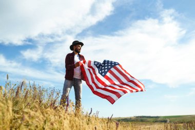 4 Temmuz. 4 Temmuz. Ulusal bayrağı olan Amerikalı. Amerikan bayrağı. Bağımsızlık günü. Vatanseverlik tatili. Adam şapka, sırt çantası, gömlek ve kot giyiyor. Güzel günbatımı ışık. 