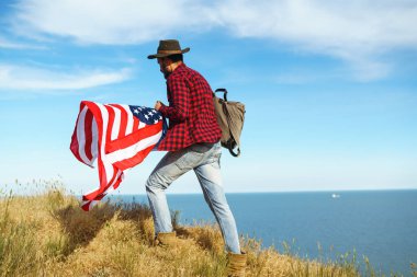 4 Temmuz. 4 Temmuz. Ulusal bayrağı olan Amerikalı. Amerikan bayrağı. Bağımsızlık günü. Vatanseverlik tatili. Adam şapka, sırt çantası, gömlek ve kot giyiyor. Güzel günbatımı ışık. 