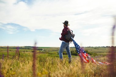 4 Temmuz. 4 Temmuz. Ulusal bayrağı olan Amerikalı. Amerikan bayrağı. Bağımsızlık günü. Vatanseverlik tatili. Adam şapka, sırt çantası, gömlek ve kot giyiyor. Güzel günbatımı ışık. 